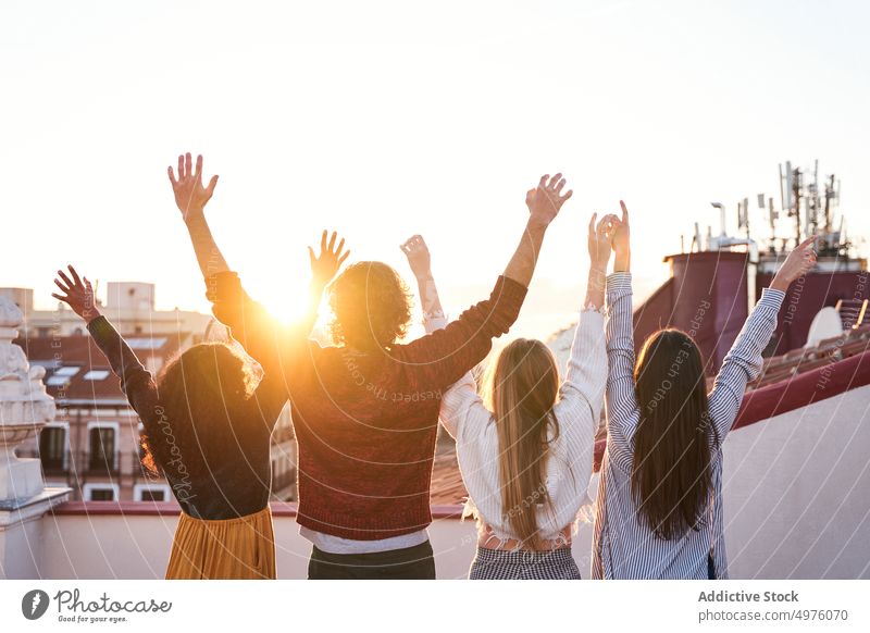 Group of unrecognizable friends celebrating and observing cityscape on terrace rooftop sunset observe admire town together arms raised twilight bonding gather