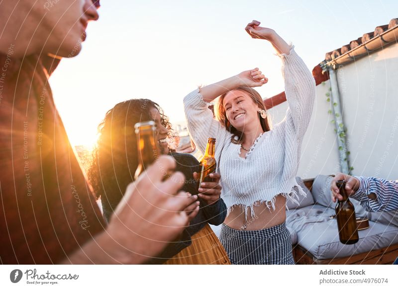 Delighted friends drinking beer and dancing on rooftop at sunset dance party booze happy carefree hangout chill beverage arms raised celebrate fun friendship