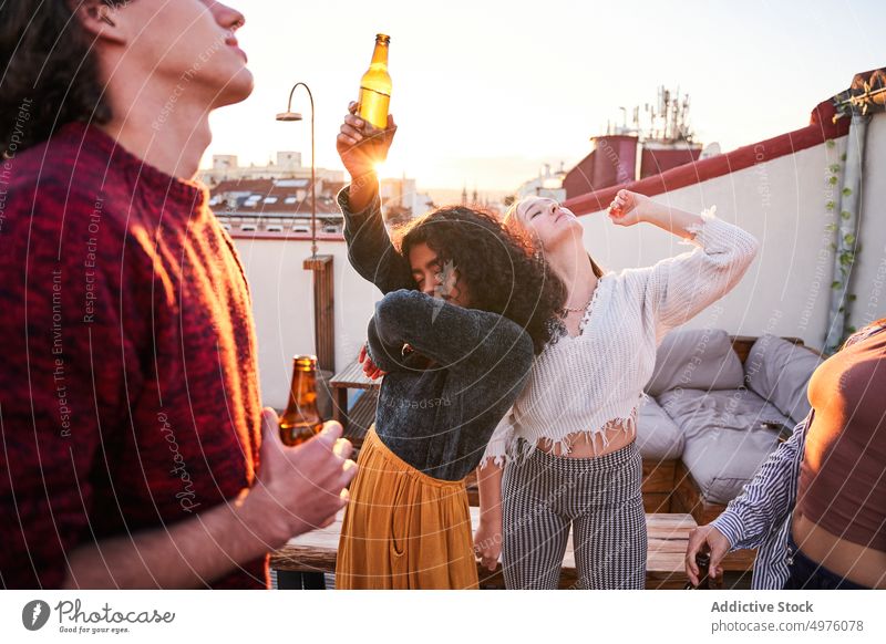Delighted friends drinking beer and dancing on rooftop at sunset dance party booze happy carefree hangout chill beverage arms raised celebrate fun friendship
