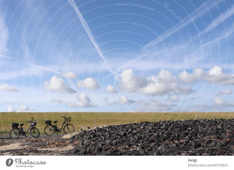 Two bicycles stand on the Elbe cycle path below the dike, in the blue sky you can see small clouds and contrails of airplanes Bicycle e-bike Pedelec Cycling
