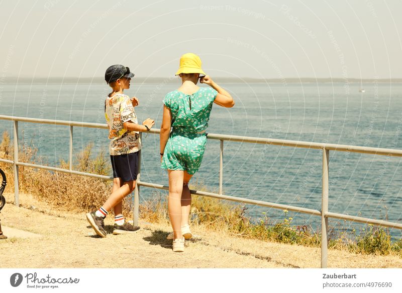 Two children in summer clothes are talking, on the railing in front of the sea Sun Summer T-shirt Dress Hat conversation exchange Ocean Warmth entertainment