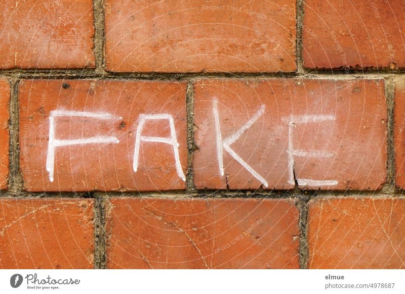 FAKE is written in white capital letters on a red brick wall fake Fraud Anglicism fakenews jargon youth language disingenuous pretence Daub Manipulation