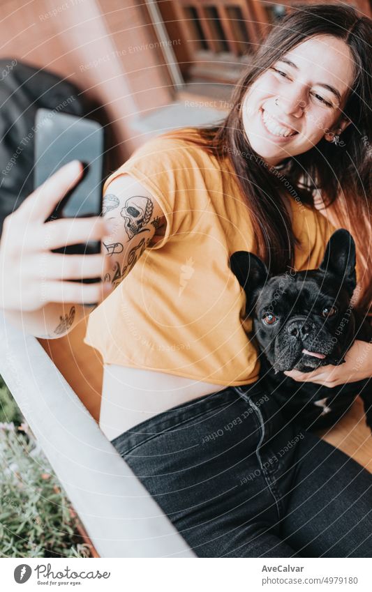 Young woman taking photo selfie cuddling and taking care of her french bulldog with tongue out on home.Puppy observing concentrated looking the city.Playful,humorous and cheerful friendship partner.