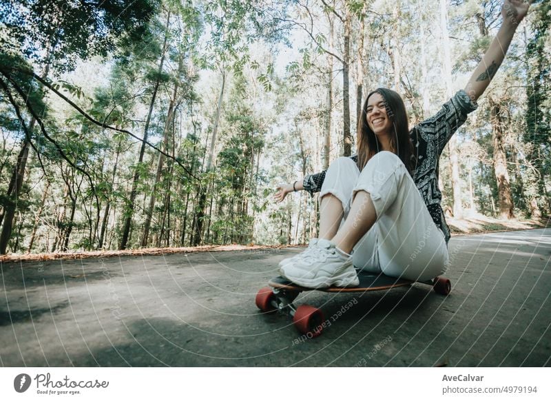 Young woman having fun descending a road in the middle of the forest with a longboard skate. Practicing outdoors and extreme sports, far away from the city. New generations and freedom concept