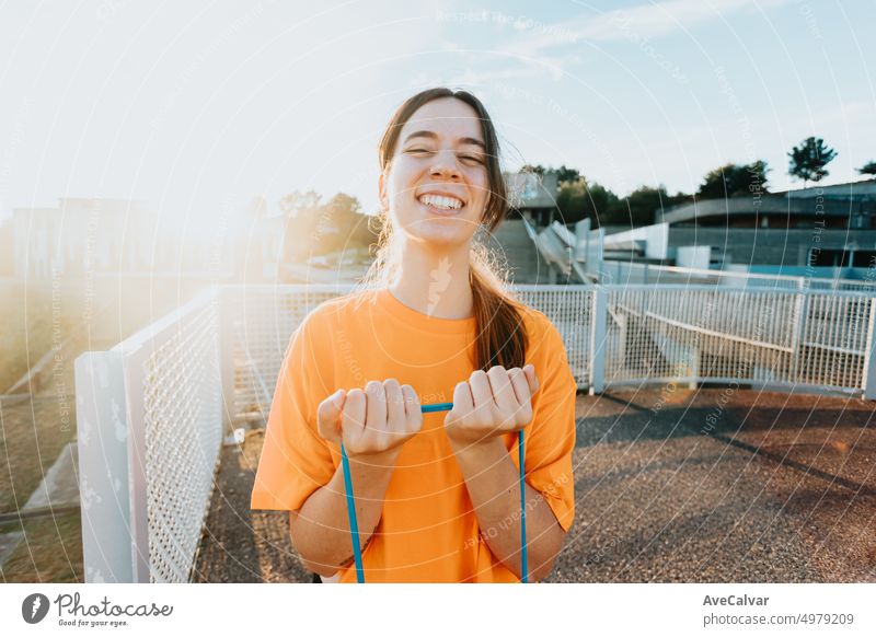 Smiley young woman working out with resistance band outdoors. Beginner girl training and performing exercises to define arm muscle. Tone and stretch the body. New sport and hobby for healthy life