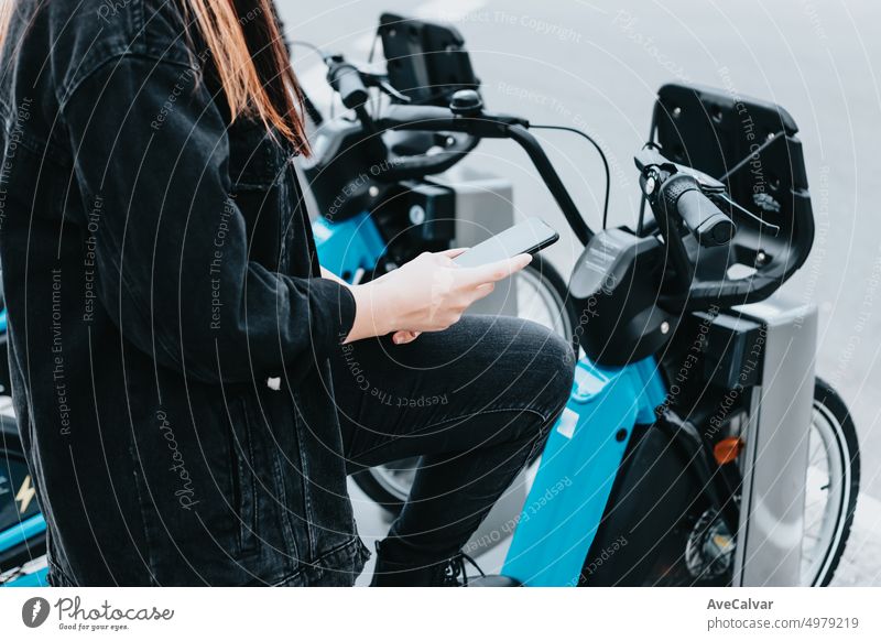 Young adult browsing on smartphone looking for rent mobile app to take a bike.Checking if there is any available bicycle and battery status.Electric transport concept.Renewable and healthy resources