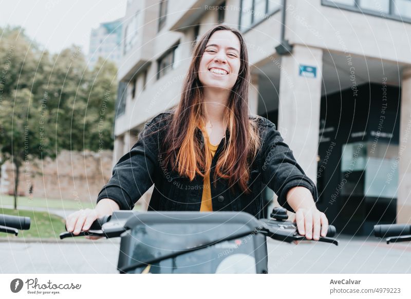Portrait of young adult renting electric bike to sightseeing the city.Different ways to move around and make tourist planning.Urban,ecological and public transport.Cheerful,smiling and excited woman