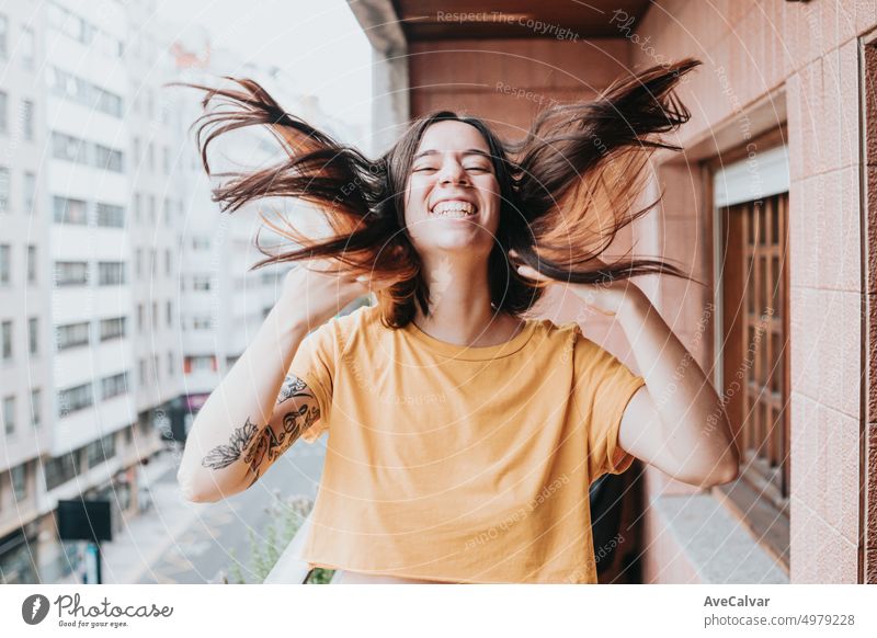Cheerful and smiling young adult woman moving hands and hair at camera.Feeling freedom and unattached.Nervous and excited for new job and experiences,city lifestyles.Laughing in terrace of new home.
