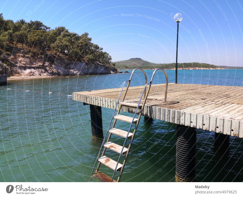 Boat jetty with ship planks and bathing ladder in summer with blue sky and sunshine at Ayvalik beach on the Aegean Sea in Izmir province, Turkey bathing jetty