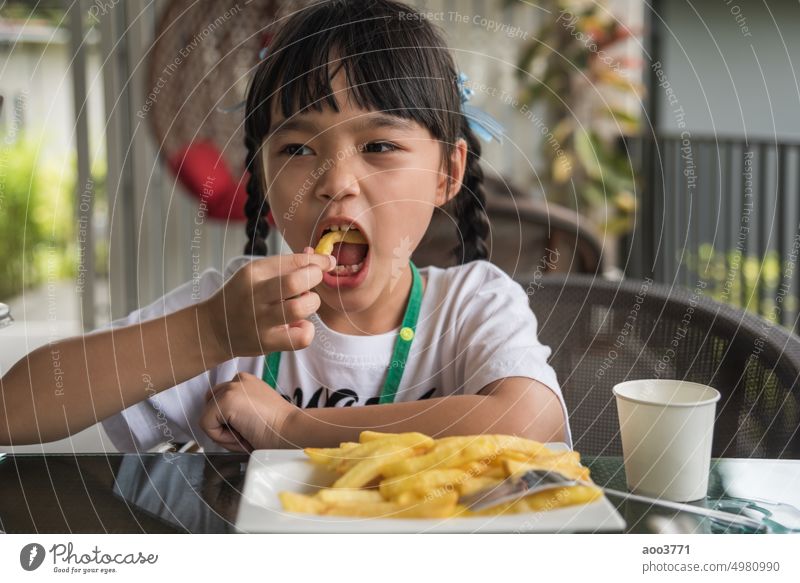 Young Asian girl eating french fries young kid fun happy potato fast food. asian little child person minor smile happiness female portrait hunger restaurant