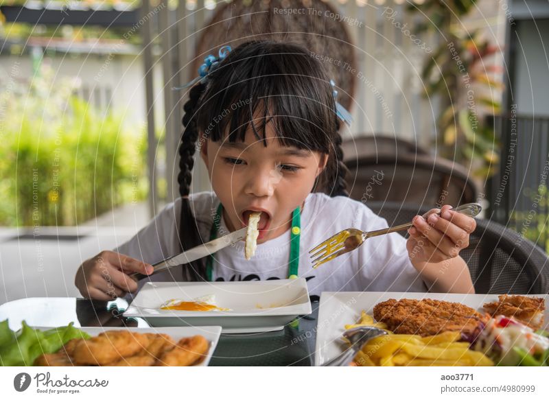 little girl asian eat fried egg on dish at table. child person fork young morning baby home smile kitchen white enjoy family fun kid kindergarten toddler dining
