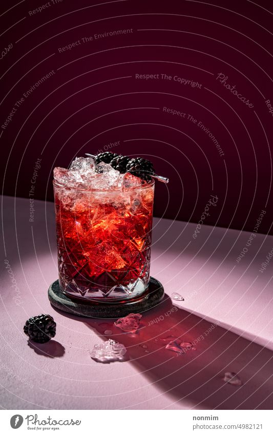 Summer cold cocktail drink with ice garnished with blackberry on dramatic violet purple red pink liquid alcohol alcoholic beverage cocktail glass cool