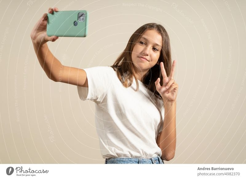 Close-up portrait of a cheerful spanish girl teenager schoolchild pupil taking selfie photo self-picture on smart phone, having video call conversation online isolated in beige background.