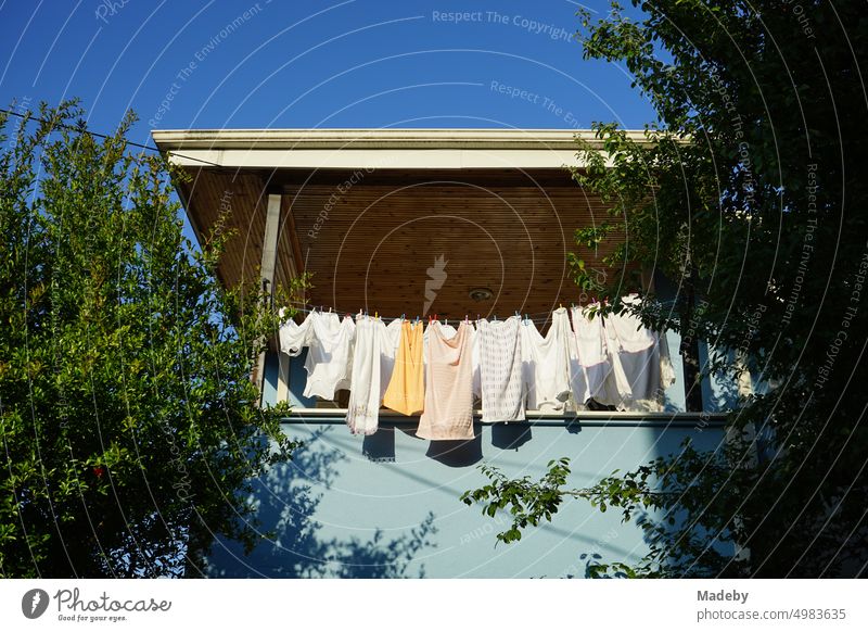 Clothesline with freshly washed clothes and underwear on the balcony and veranda of an old residential house against blue sky in the sunshine in Adapazari, Sakarya province, Turkey