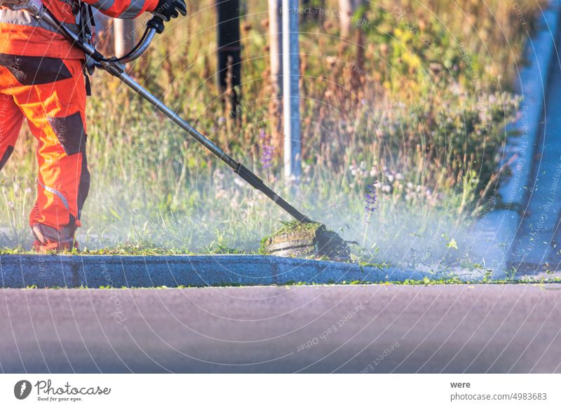 a worker removes wild weeds in a dust cloud at the roadside with a string mower Road clean gardening maintain nature nobody noisy technology traffic