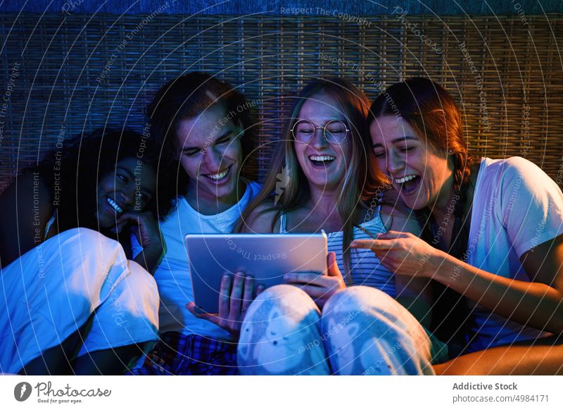 Laughing friends watching funny video in dark bedroom laugh tablet joyful night entertain device gadget together using flatmate movie surfing cheerful at home