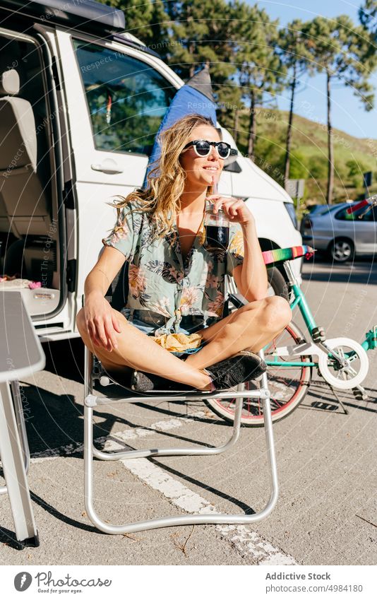 Cheerful woman enjoying a juice while sitting out of caravan in camping journey trip transportation vacation adventure travel summer camper recreation leisure