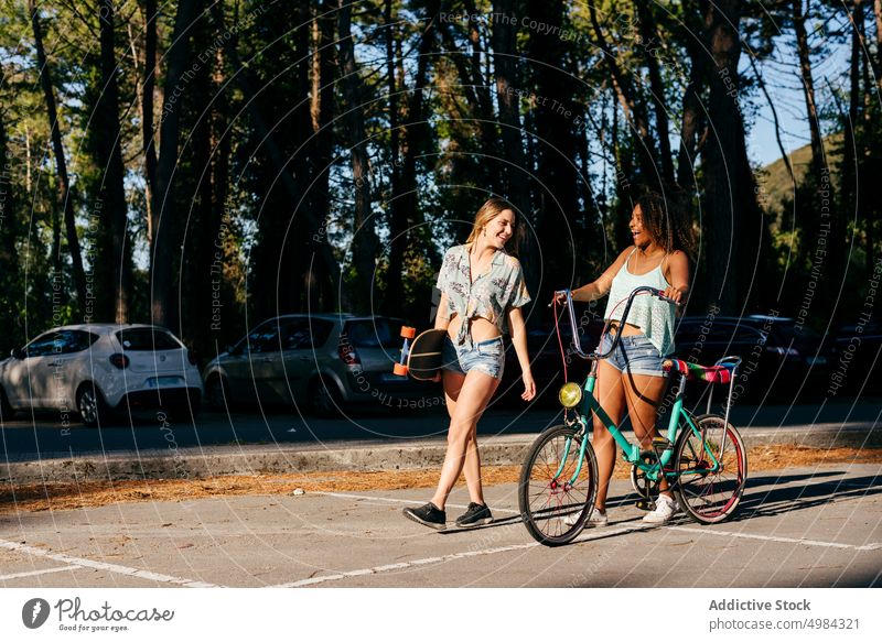 Female friends walking on street holding skate board and bicycle skateboard city laughing happiness horizontal smiling enjoy 20s fun youth lifestyle urban