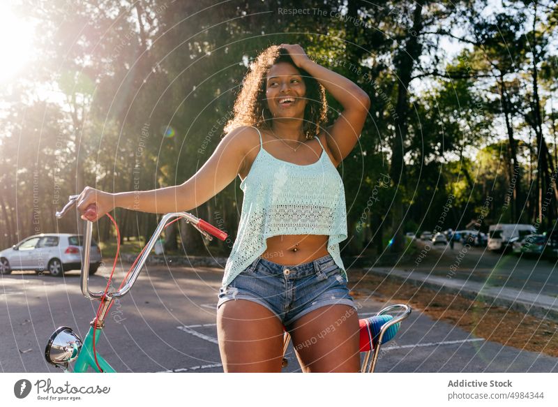 Woman smiling and looking away while sitting on a bike summer bicycle happy person young one pretty ethnicity african lifestyle portrait park female outside