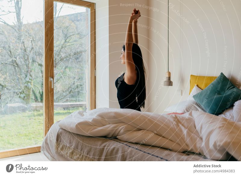 Charming Hispanic lady with upped hands on bed near window bedroom hispanic charming woman attractive young beautiful slim light looking sitting cozy home rest