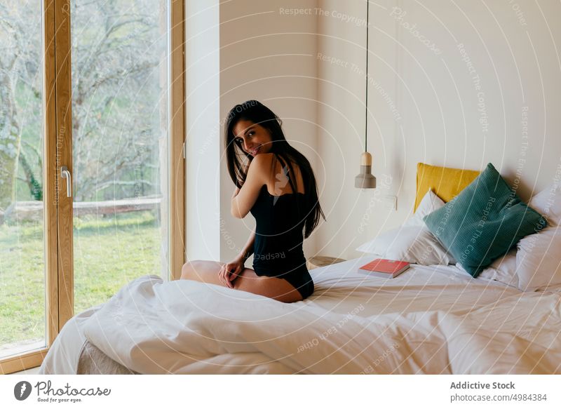 Charming Hispanic lady on bed near window bedroom hispanic upped hand charming woman attractive young beautiful slim light looking sitting cozy home rest relax