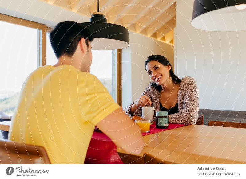 Young couple having breakfast at table cup chair window hispanic room woman mug juice drink smiling young beautiful happy court sitting attractive cozy home