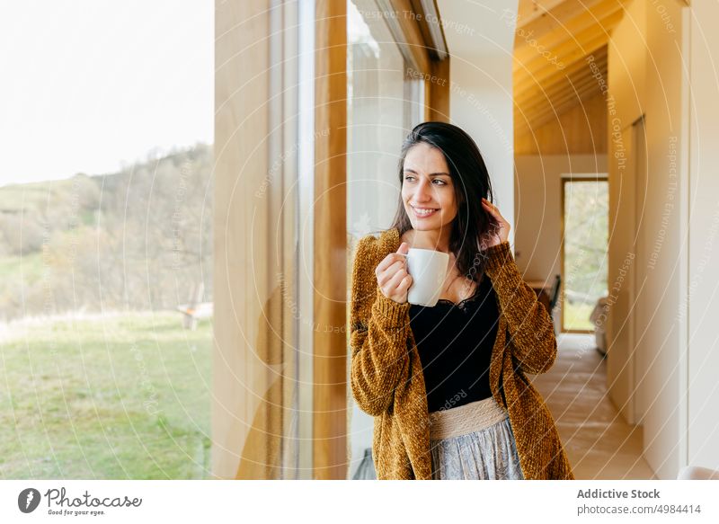 Young woman with cup near window in room hispanic lady attractive mug drink young big beautiful court cozy home rest relax beverage liquid lovely charming