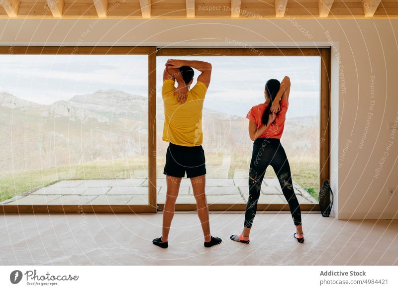Slim lady and guy standing in room stretching plank sport sportswear woman athletic slim active window activity gymnastic panorama mountain view countryside
