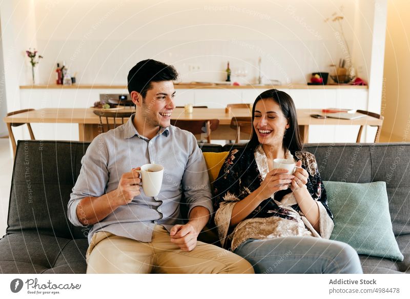 Happy couple with cup and plate on sofa in room happy hispanic kitchen mug settee cheerful smiling woman young attractive beverage drink comfort meal studio