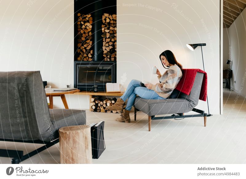 Young woman sitting on armchair with book near fireplace and window in room hispanic lady volume chimney reading attractive young big beautiful court cozy home