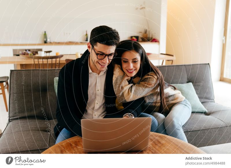 Man using laptop near happy woman on sofa couple hispanic typing eyeglasses settee young attractive room device gadget browsing cheerful connection comfort
