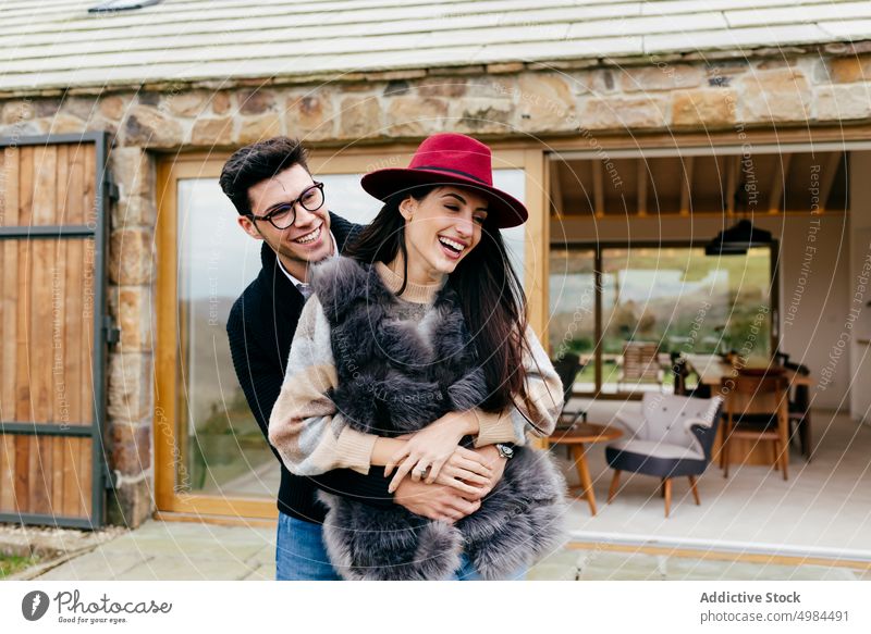 Happy couple hugging near modern house happy hispanic woman embracing eyeglasses back hat cottage smiling cheerful young attractive romantic love elegant