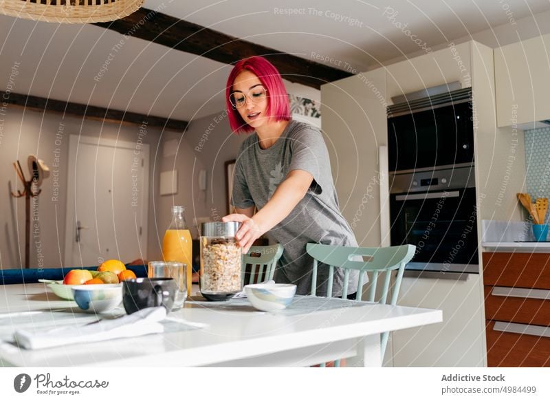 Young woman preparing breakfast at home morning cereal prepare kitchen apartment modern domestic female young jar dyed hair pink informal subculture meal cook