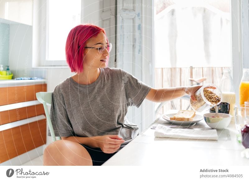Young lady having healthy breakfast at home woman spilling oatmeal morning smile table cozy eat kitchen apartment modern female young pink hair dyed hair