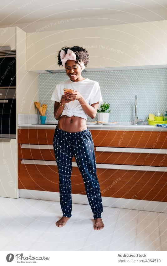 Cheerful black woman using smartphone in kitchen smile apartment modern style ethnic cozy female lifestyle home relax young domestic cheerful joy device gadget