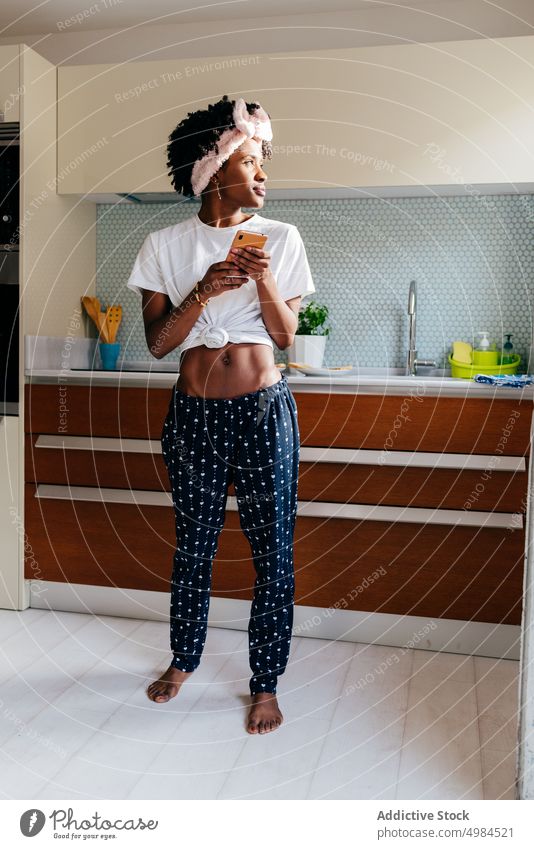 Cheerful black woman using smartphone in kitchen smile apartment modern style ethnic cozy female lifestyle home relax young domestic cheerful joy device gadget
