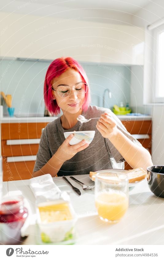 Young lady having healthy breakfast at home woman morning smile table cozy eat kitchen apartment modern female young pink hair dyed hair alternative lifestyle