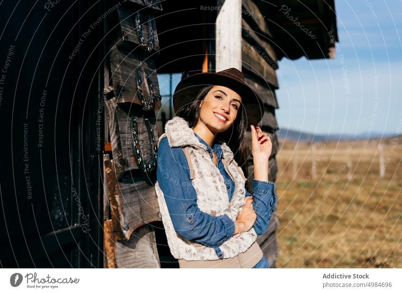 Stylish woman in hat on ranch confident style cheerful house porch cowgirl vest brunette sunlight attractive casual lifestyle beauty trendy model freedom