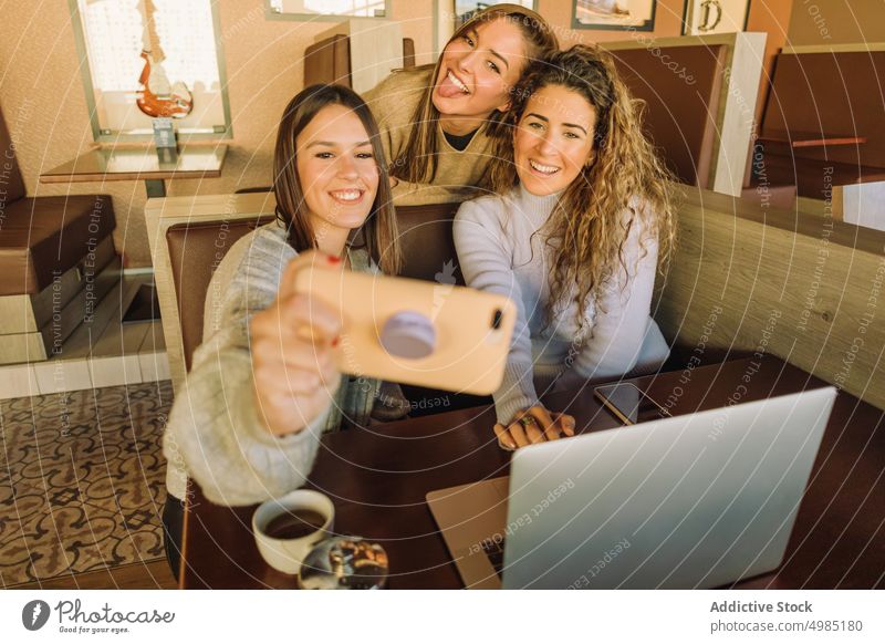 Positive friends taking selfie in cafe women take photo smartphone positive fun girlfriend table laptop female tongue out gadget device netbook share tea happy