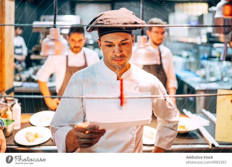 Man reading orders on paper working in kitchen chef list culinary restaurant staff menu professional job meal commercial dinner modern standing occupation food