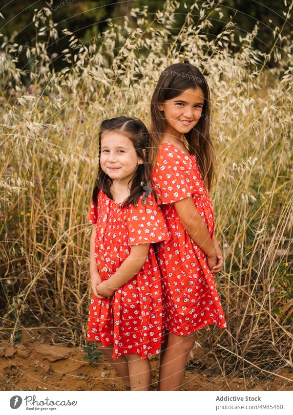 Smiling girls standing on meadow with high grass sister summer happy nature field childhood red dress vacation expression fun friend similar family together