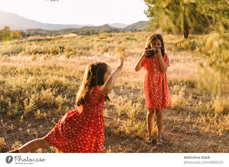 Girl taking photo of little sister in meadow girl friendship summer field nature camera photography happy beautiful technology adorable red child enjoyment