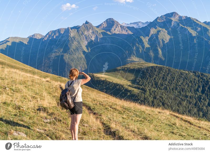 Unrecognizable woman standing on grassy hill slope against rocky mountains highland admire picturesque severe range backpacker hiker pyrenees spain scenery