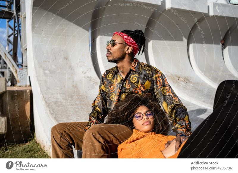 Black couple on bench in modern city square laugh happy urban embrace cuddle date together ethnic black african american relationship cheerful rest dreadlocks