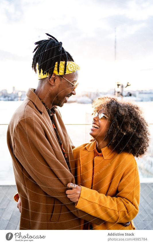 Stylish black couple in coats on city promenade pier trendy urban colorful autumn style laugh ethnic african american fashion afro dreadlocks hairstyle yellow