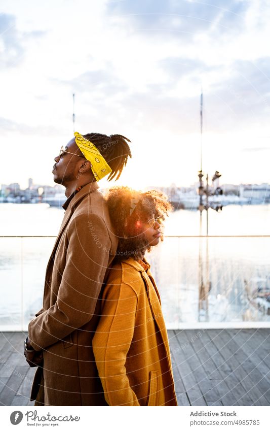 Stylish black couple in coats on city promenade pier trendy urban colorful autumn style ethnic african american fashion afro dreadlocks hairstyle yellow