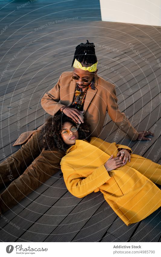 Sensual fashionable couple on wooden floor trendy colorful love caress together dream ethnic black african american afro dreadlocks coat autumn cuddle harmony