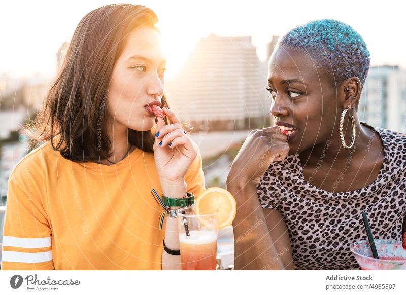 Multiethnic couple of cool lesbian women drinking cocktails summer tropical eat candy lgbt refreshment girlfriend multiethnic multiracial diverse black