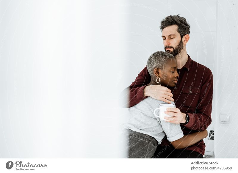 Gentle multiethnic couple cuddling in morning time together hug kitchen love happy cozy close coffee cuddle home relationship casual embrace romantic affection