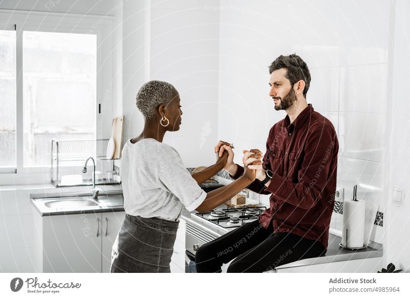 Pleased multiethnic lovers holding hands in kitchen couple hug cuddle sit cabinet home relationship smile affection laugh tender casual embrace sensual together